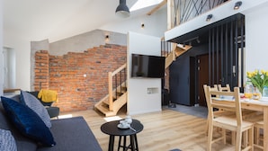 Un espace de vie moderne avec un mur en briques, un escalier, un téléviseur à écran plat, un coin repas avec des meubles en bois et un canapé avec des coussins.