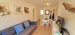A living room with a sofa, a dining table with chairs, a TV, and artwork on the walls.
