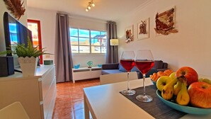 Un soggiorno moderno con un tavolo da pranzo per due persone, con una ciotola di frutta e due bicchieri di vino rosso.