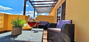 An outdoor seating area with a table, two chairs, a potted plant, candles, and two glasses of red wine.