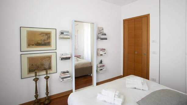 Une chambre à coucher avec un lit, une armoire en bois, un miroir et des œuvres d’art encadrées accrochées au mur.