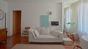 Un salon avec un canapé blanc, une petite table, un téléviseur et une porte donnant sur une autre pièce.