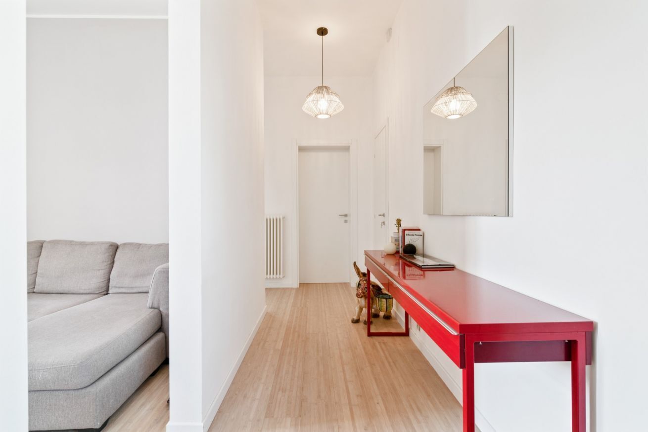 Un couloir avec un canapé, une console rouge et deux lampes suspendues.