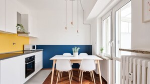 Una cucina moderna con mobili bianchi, un piano di lavoro giallo, una parete decorata in blu, un tavolo da pranzo con sedie e un lampadario.