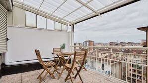 Un balcone con tavolo e sedie, una pianta in vaso e vista sulla città.