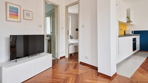 Un appartamento moderno con una TV su un mobile bianco, pavimento in legno, cucina con mobili bianchi e una parete d'accento blu.