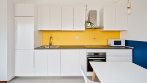 Una cucina moderna con mobili bianchi, uno schienale giallo, un forno a microonde e un lavello.