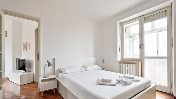 Una camera da letto moderna con un ampio letto, comodini, una TV e una finestra con persiane.