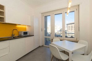 A modern kitchen with a microwave, white cabinets, a dining table with chairs, and large windows offering a city view.