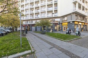 A multi-story building with a ground-level commercial space, a pedestrian pathway, and parked scooters.