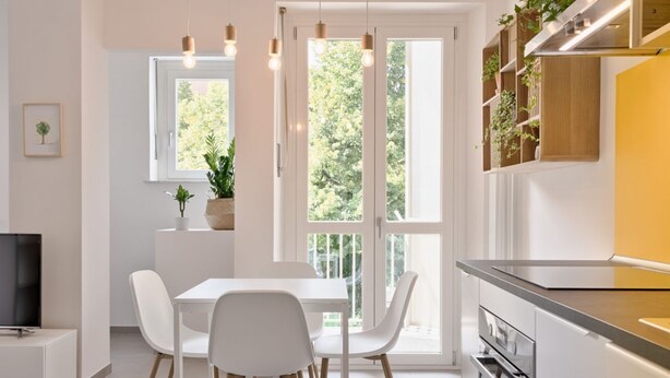A modern kitchen with white cabinetry, a dining table with chairs, a built-in oven, and a window with a view of greenery. - GuestHost - Comfortable studio perfect for 2 guests is located near the famous Parco del Valentino with the beautiful castle and the medieval village, a few subway stops from the historic center, near the famous Eataly, the Lingotto, the Molinette Hospit (Torino)