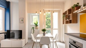 A modern kitchen with white cabinetry, a built-in oven, and a dining area with a white table and chairs.