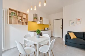 Une cuisine moderne avec des meubles blancs, un mur d’accent jaune et un coin repas comprenant une table et des chaises blanches.