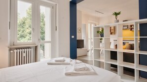 A bedroom with a bed, a radiator, a window, and a shelving unit with plants.
