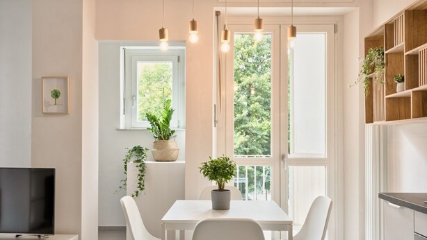 A modern kitchen with white cabinetry, a dining table with chairs, a TV, and a window with a view of greenery.