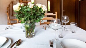 Une table à manger dressée avec de l’argenterie, des couverts et des verres à vin, et un vase de roses blanches placé au centre.