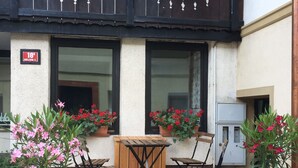 Une terrasse extérieure en bois, avec une table et des chaises, entourée de plantes et de fleurs en pot.