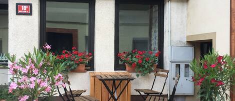 Una terraza de madera al aire libre con una mesa y sillas, rodeada de macetas con plantas y flores.