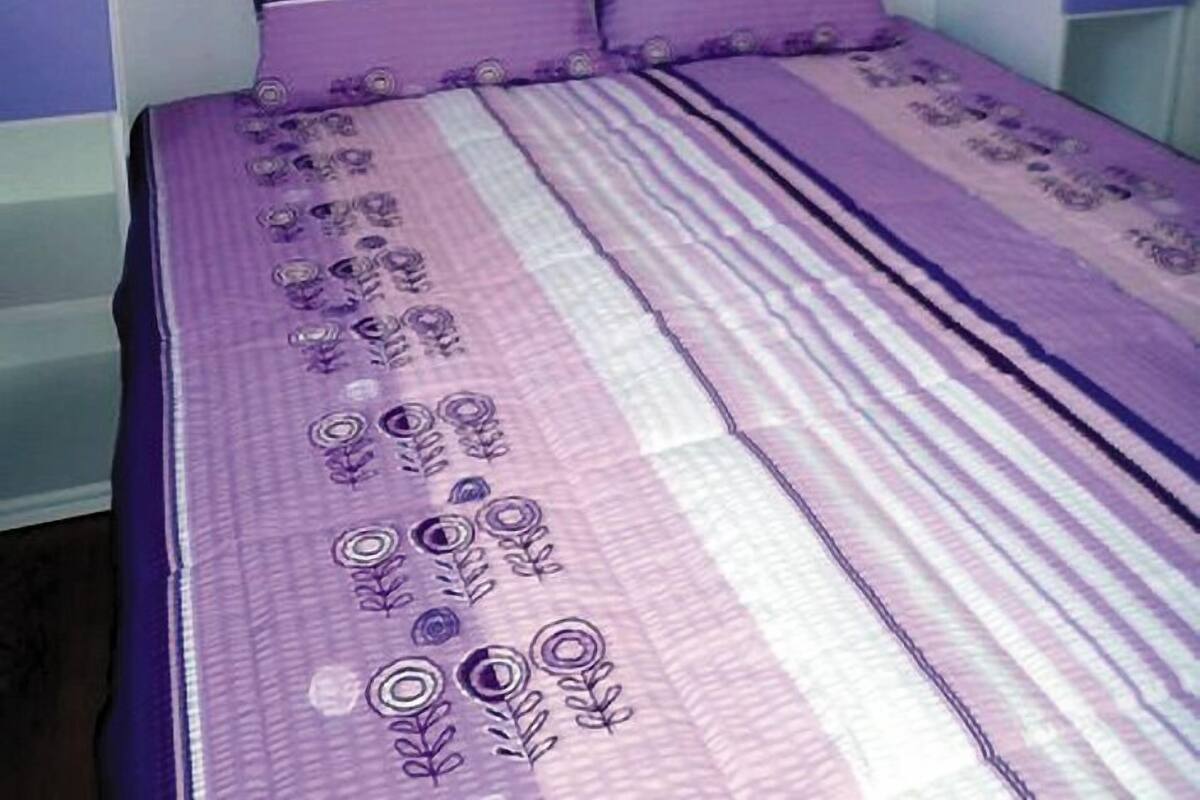 Un lit avec une couvre-lit à rayures violettes et blanches et des oreillers assortis.