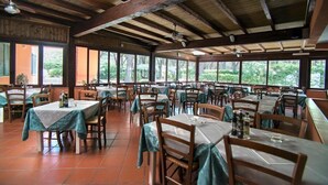 A spacious restaurant with wooden beams and large windows offering views of greenery. Tables are neatly arranged with chairs, and the floor is tiled. - Victoria Mobilehome Camping Ville Degli Ulivi (Campo nell'Elba)