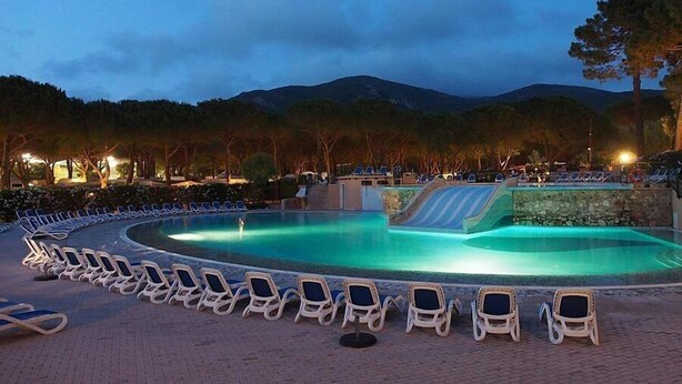 A swimming pool with lounge chairs and a water slide, surrounded by trees and mountains. - Victoria Mobilehome Camping Ville Degli Ulivi (Campo nell'Elba)
