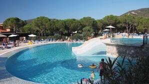 A pool area with lounge chairs, a water slide, and a stone wall. - Victoria Mobilehome Camping Ville Degli Ulivi (Campo nell'Elba)
