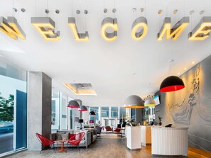 Un área de recepción moderna con un letrero que dice 'WELCOME', asientos, un mostrador de recepción y ventanas amplias.