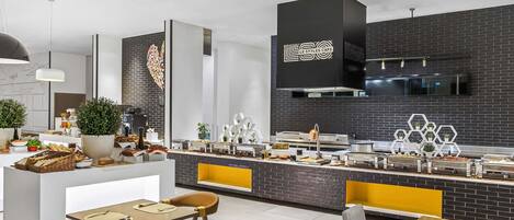 A modern cafe with a black brick wall, a central counter with food displays, and yellow and black striped chairs.