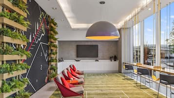 Un área de descanso moderna con alfombra temática deportiva, una gran pantalla de televisión y una pared cubierta de plantas trepadoras.