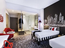 Habitación de hotel moderna con cama, escritorio, silla, espejo y una pintura de un paisaje urbano en la pared.