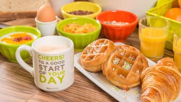 Una mesa de desayuno con waffles, un croissant, una taza y varios cuencos de comida.
