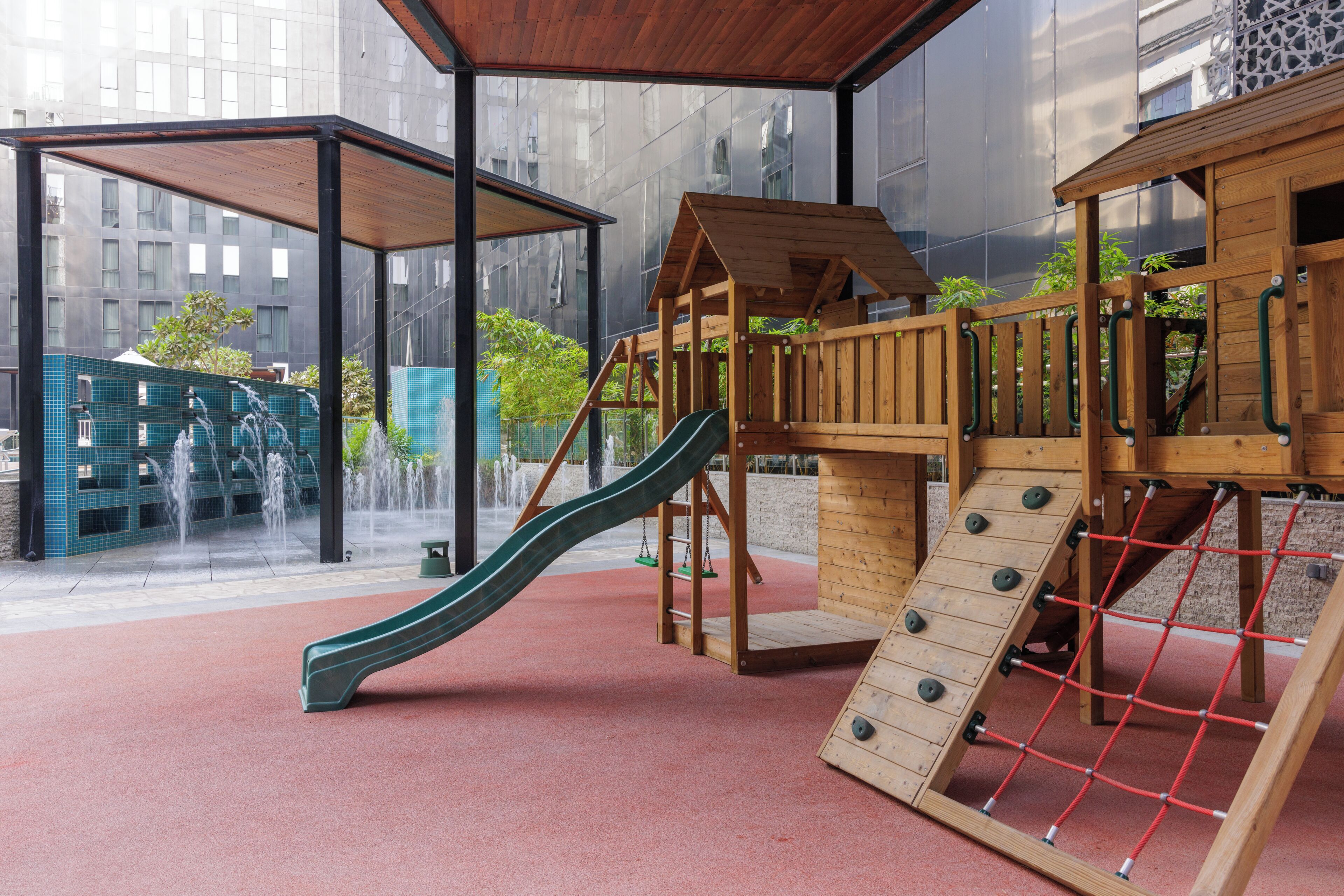 Zona de juegos infantiles con tobogán, red de escalada y estructuras de madera.