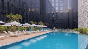 A swimming pool with lounge chairs and umbrellas, surrounded by modern buildings. - ibis Styles Dubai Airport Hotel (Dubai)