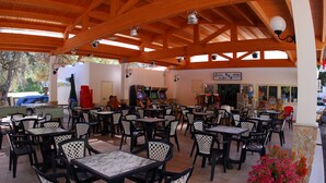 An outdoor cafe with multiple tables and chairs, a vending machine, and a sign for a nearby business. - Victoria Mobilehome Stella del Sud Camping Villaggio (Rodi Garganico)