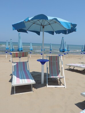 Una playa con sillas reclinables a rayas y sombrillas azules.