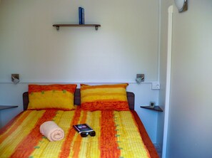 Una cama con colcha a rayas, dos almohadas, una toalla enrollada y un libro con gafas de sol encima.