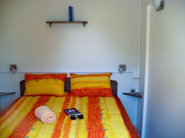 A bed with a striped bedspread, two pillows, a rolled towel, and a book with sunglasses on it.