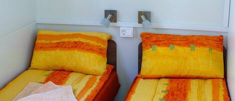 Two single beds with orange and yellow striped bedding, a small shelf above, and a book on the right bed.