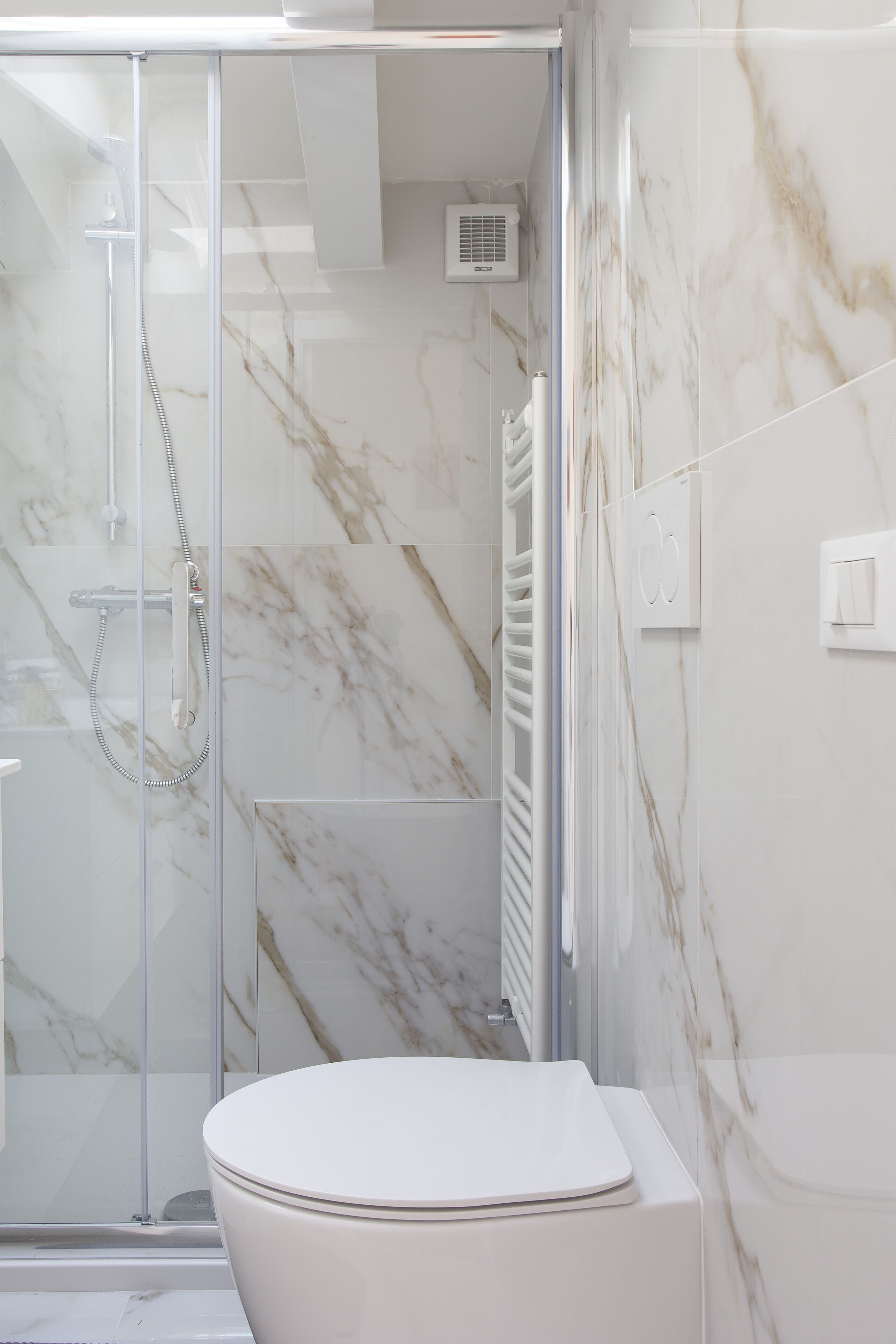 Une salle de bain avec une douche à parois de verre, des toilettes blanches et des murs à motifs de marbre.