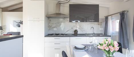 Une cuisine moderne avec des meubles blancs, un pare-feu en marbre et un coin repas avec une table dressée pour quatre personnes.