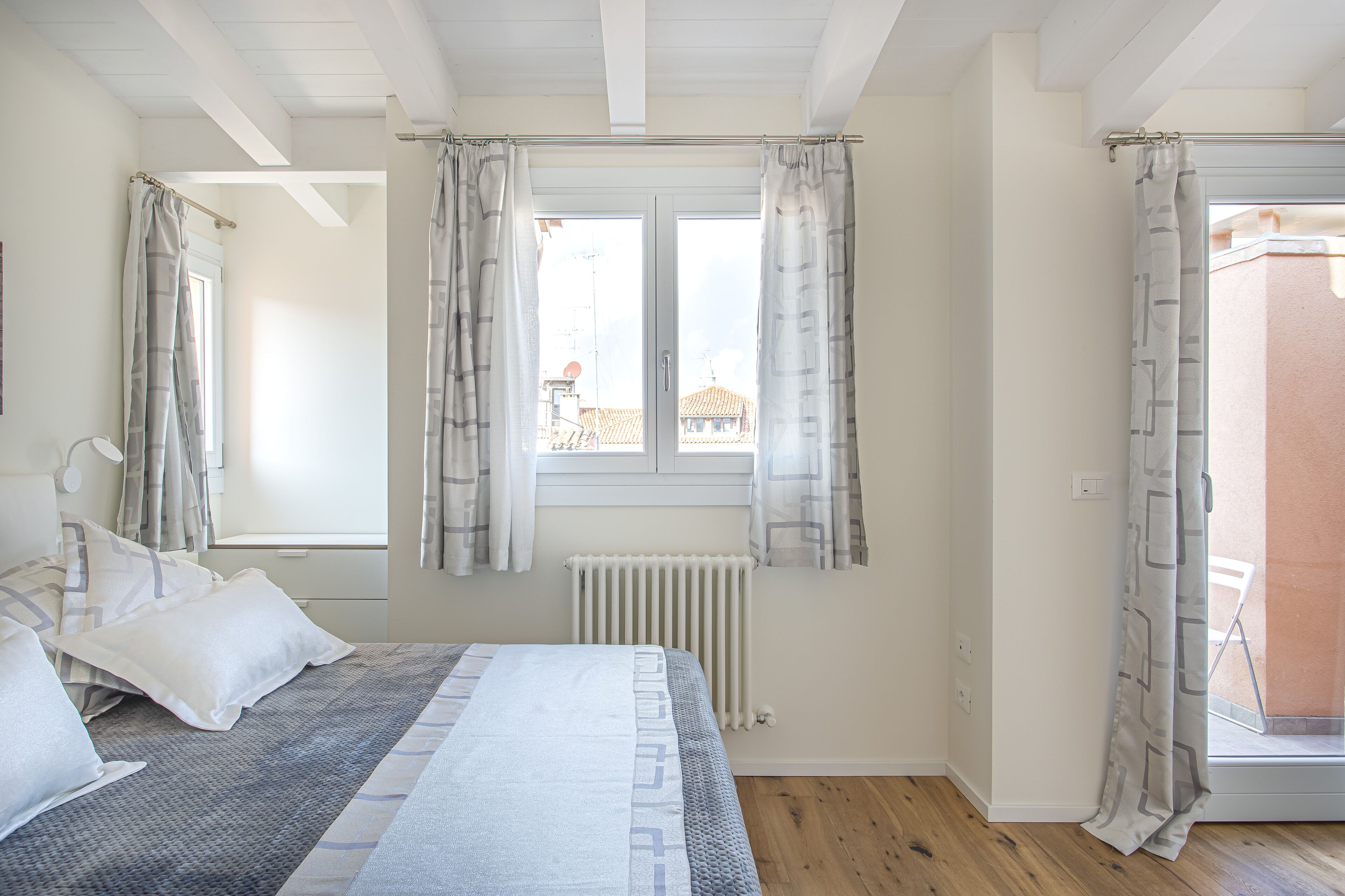 A bedroom with a bed, a window with curtains, a radiator, and a wooden floor.