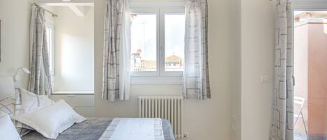 A bedroom with a bed, a window with curtains, a radiator, and a wooden floor.