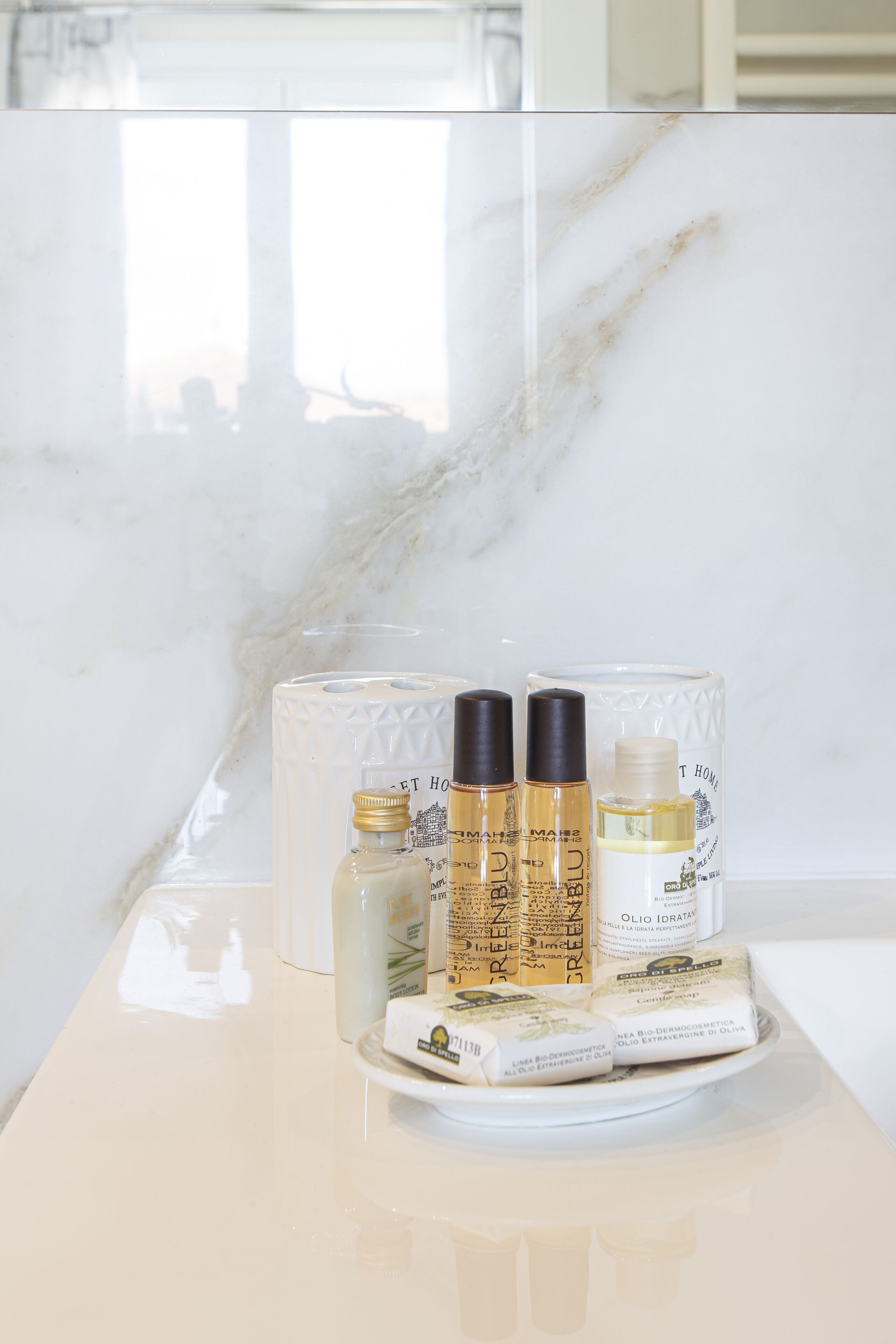 Un meuble-lavabo de salle de bain avec un plan de toilette en marbre, un récipient en verre et deux bouteilles d’huile d’olive.
