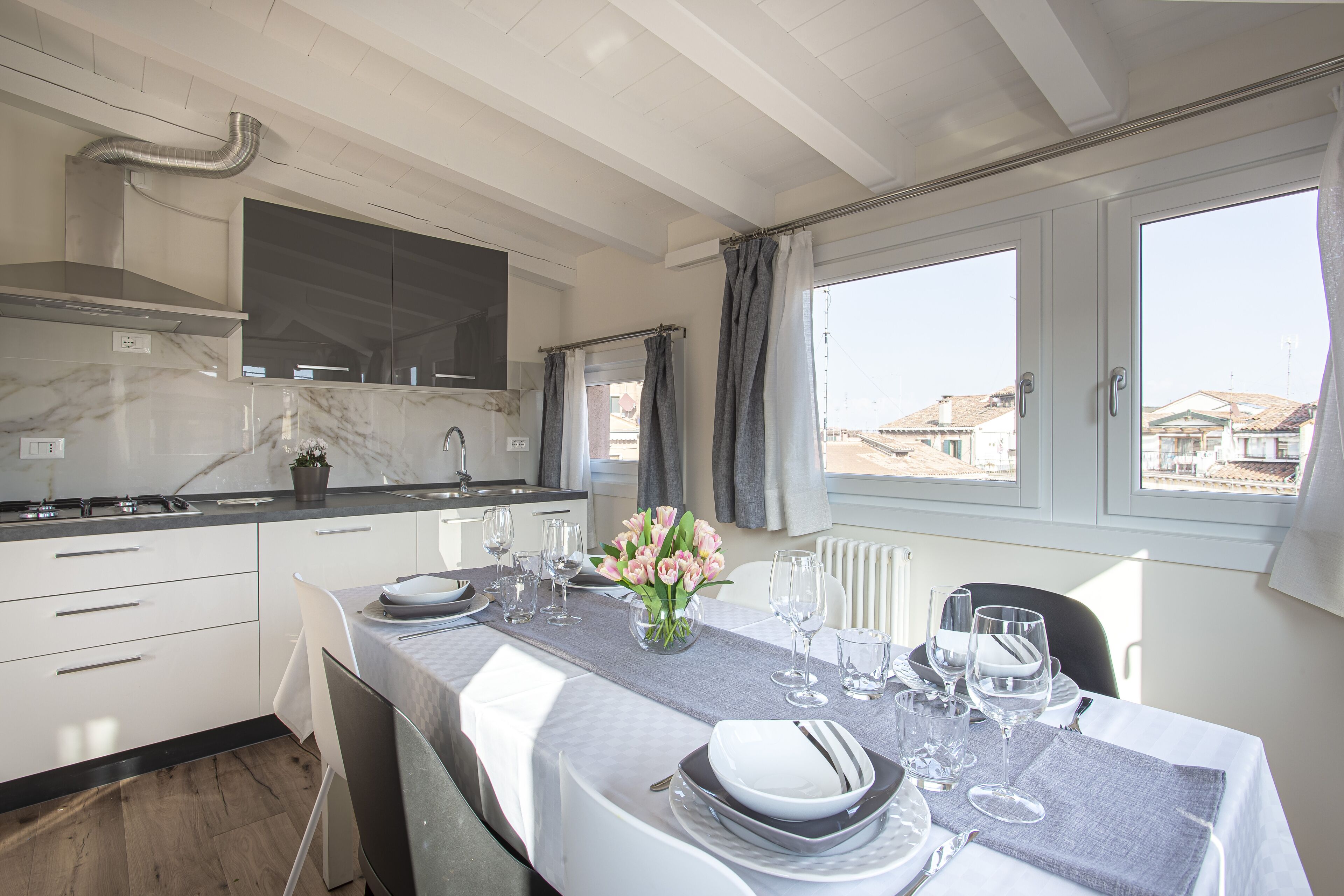 A modern kitchen with white cabinets, a marble countertop, and a dining area set for six with a table set for a meal.