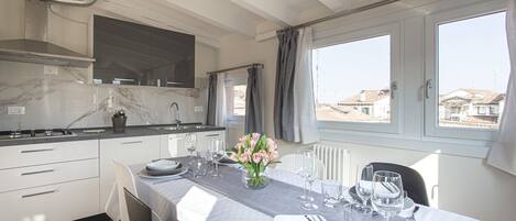 A modern kitchen with white cabinets, a marble countertop, and a dining area set for six with a table set for a meal.