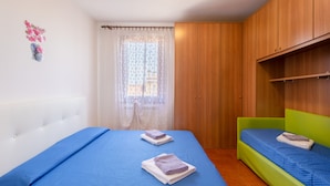 Un dormitorio con dos camas, un armario de madera y una ventana con cortinas de encaje.
