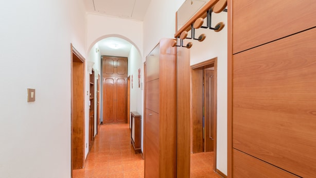 Un pasillo con puertas de madera, suelo de baldosas y una lámpara en el techo.