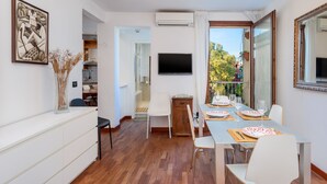 A modern dining area with a wooden table set for four, a television mounted on the wall, and a view of the outside through large windows. - Venice Rio dei Greci San Marco (Venice)