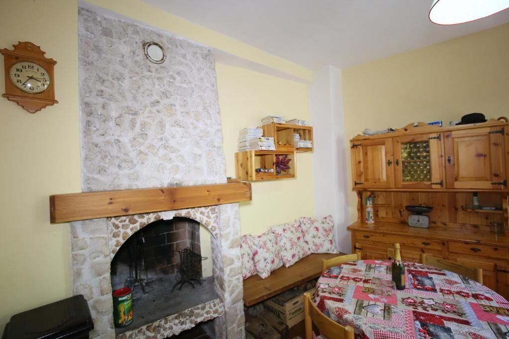 A cozy room with a stone fireplace, wooden shelves, a wooden cabinet, and a quilt-covered table.