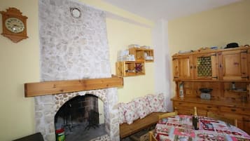 A cozy room with a stone fireplace, wooden shelves, a wooden cabinet, and a quilt-covered table.